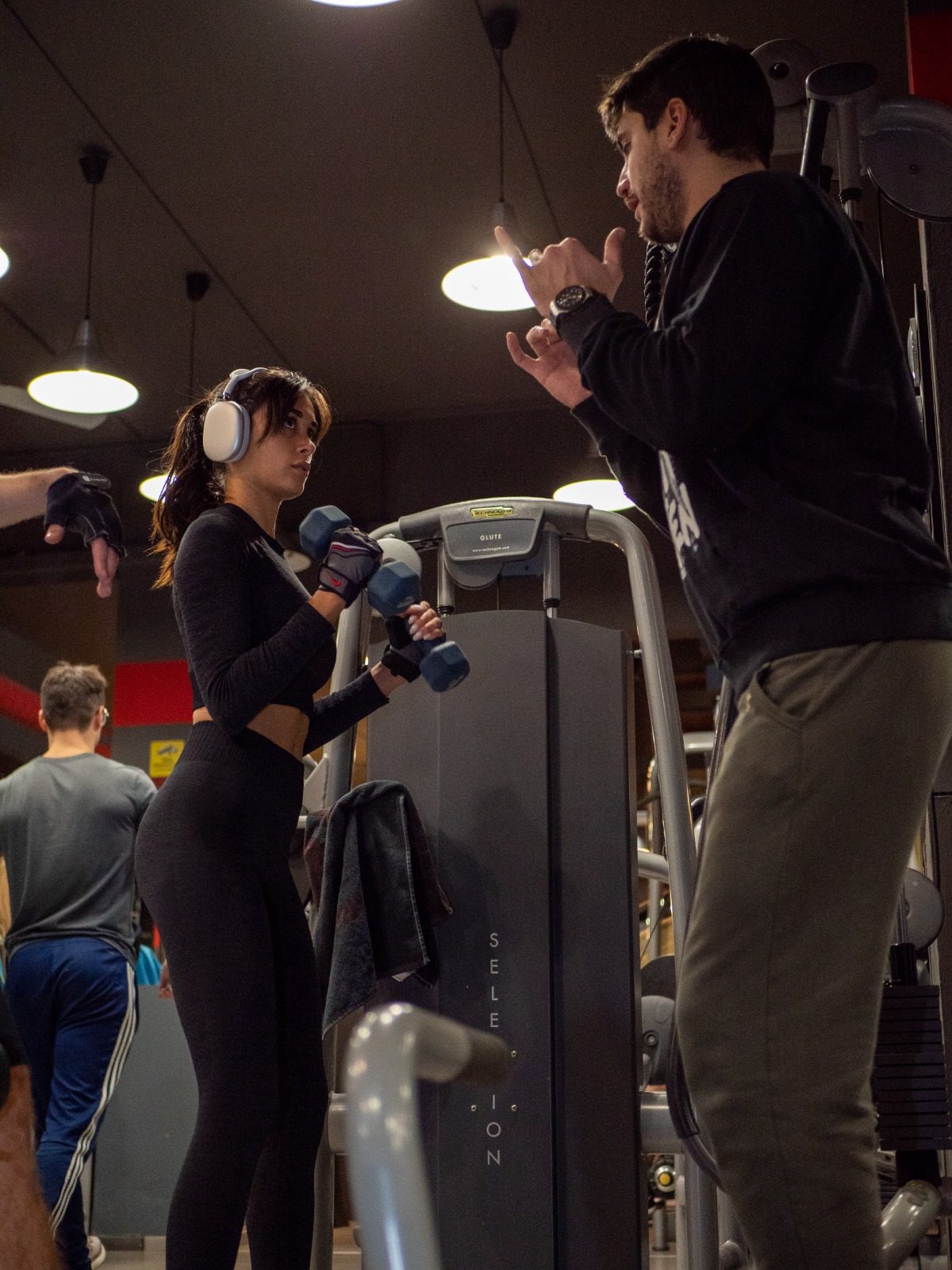 Un personal trainer segue un'allieva con i manubri accanto a una macchina Technogym.